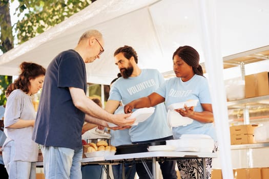 Multiracial team working together at food drive, charitably distributing essential items to less fortunate. Multiethnic people wearing blue t-shirts providing hunger relief and volunteer assistance.