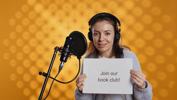 Joyous woman filming promotional video for world book day using microphone, studio background. Happy content creator promoting reading, gaining awareness for literature importance, camera B