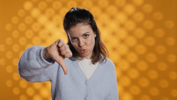 Disappointed woman bashing book, showing thumbs down hand sign, isolated over studio background. Upset bookworm dissatisfied with new novel, giving negative review, camera B