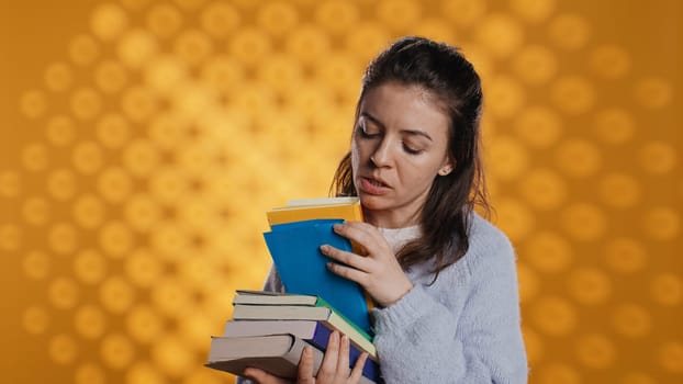 Excited woman browsing though pile of purchased books, picking what to read. Enthusiastic bookaholic person looking through stack of novels to spend leisure time with, studio background, camera B