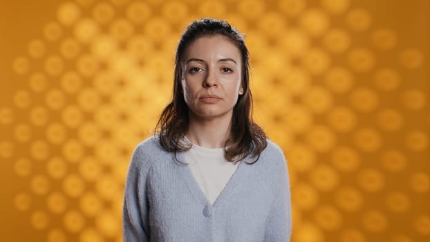 Portrait of relaxed woman posing, looking at camera, isolated over yellow studio background. Caucasian person dressed in casual attire standing, feeling confident, camera B