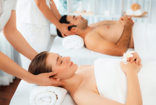 Caucasian couple enjoying relaxing anti-stress head massage and pampering facial beauty skin recreation leisure in dayspa modern light ambient at luxury resort or hotel spa salon. Quiescent