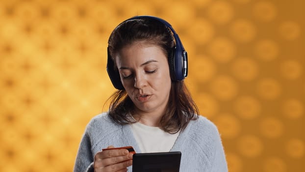 Woman reading ebook on ereader and listening music purchasing books online. Person with tablet looking to buy digital novel with credit card, hearing songs in headphones, studio background, camera A