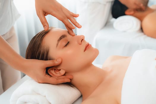 Caucasian couple enjoying relaxing anti-stress head massage and pampering facial beauty skin recreation leisure in dayspa modern light ambient at luxury resort or hotel spa salon. Quiescent