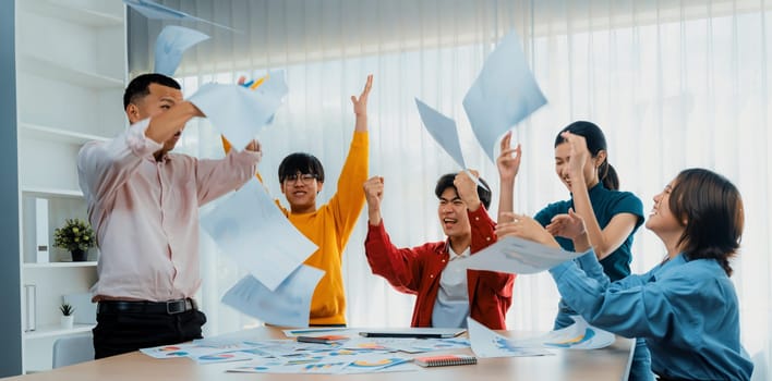 Excited and happy startup company employee celebrate and throw paper in the air after make successful business. Teamwork and positive environemtn create productive and supportive workplace. Synergic