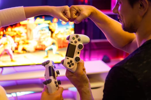 Close up of hands couple or friends joyful player video game on TV using joysticks with raising hand fist up together for winner with blurry screen in studio room in neon cyber light bulb. Postulate.