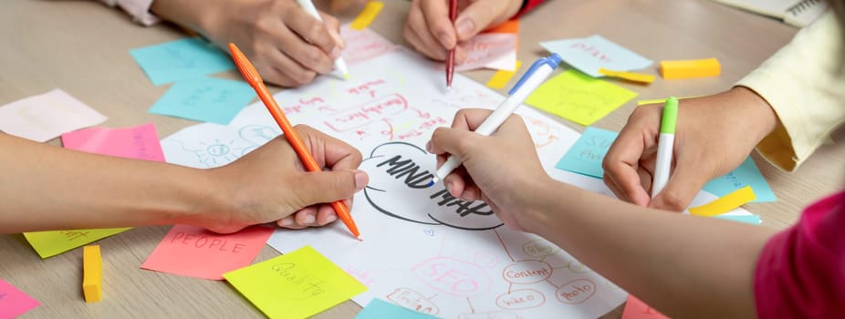 Professional startup group share creative marketing idea by using mind map. Young skilled business people brainstorm business plan while writing sticky notes. Focus on hand. Closeup. Variegated.