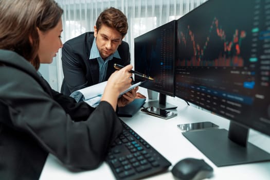 Two business traders discussing value business statistic graph company on paper report analyzing with dynamic stock exchange market currency real time website surround pc screens at office. Postulate.
