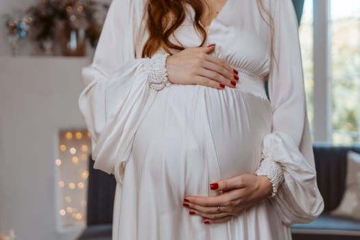 A pregnant woman is wearing a white dress and holding her stomach. Concept of anticipation and excitement for the upcoming arrival of the baby