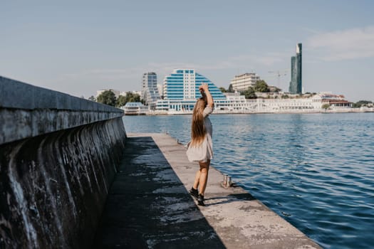 woman in a white dress is walking on a pier near the water. The scene is peaceful and serene, with the woman's long hair blowing in the wind