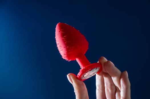 Woman holding red anal plug in water drops on blue background