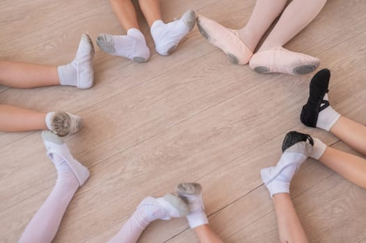 Top view of the legs of little ballerinas sitting on the floor in a circle