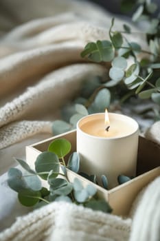 A candle is lit in a box with green leaves. The candle is surrounded by a white blanket and a green leaf. Generative AI