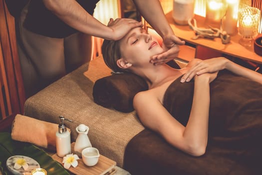 Caucasian woman enjoying relaxing anti-stress head massage and pampering facial beauty skin recreation leisure in warm candle lighting ambient salon spa in luxury resort or hotel. Quiescent