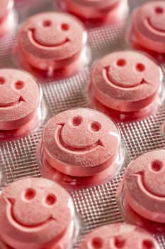 A row of pink pills with smiling faces on them. The pills are in a plastic container. Generative AI