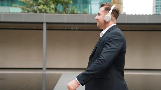 Happy project manager with headphone walking workplace while moving to relaxed music. side view of smart caucasian businessman going to meeting while dancing and walking along the city street. Urbane.