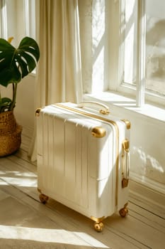 A white suitcase with gold accents sits on a wooden floor in front of a window. The sunlight shining through the window casts a warm glow on the suitcase, making it look inviting and luxurious. Generative AI