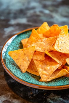 A plate of tortilla chips is on a blue plate. The chips are arranged in a triangular pattern. Generative AI