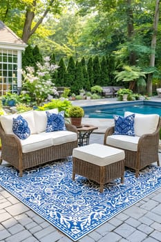 A blue and white patio set with a blue and white rug. The patio set includes a couch, two chairs, and an ottoman. The outdoor furniture is arranged around a pool, creating a relaxing. Generative AI