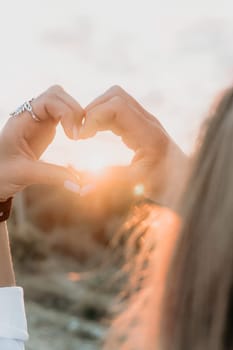 A woman's hand is holding a heart shape, with the sun shining on it. Concept of love and warmth, as the sun symbolizes happiness and positivity. The heart shape represents the bond between two people