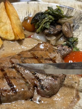 Sirloin steak grilled medium rare served with potatoes and salad with mushroom black pepper sauce in a restaurant