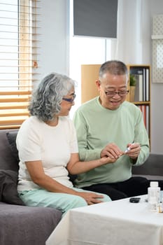 Caring mature man checking blood sugar of his diabetic wife at home. Elderly healthcare concept.