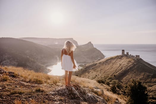 A woman stands on a hill overlooking a body of water. The sky is clear and the sun is shining brightly. The woman is enjoying the view and the peaceful atmosphere