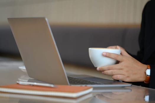 Businesswoman holding a white cup of coffee using laptop at cafe.