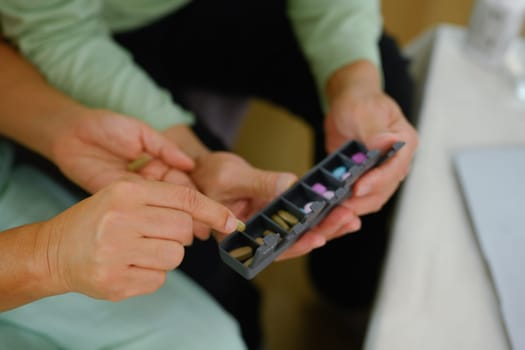 Closeup elderly woman putting pills into pill organizer. Health care, medicine and treatment concept