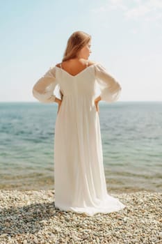 woman white dress stands on a beach, looking out at the ocean. She is in a contemplative or reflective mood, as she raises her hands above her head. Concept of peace and tranquility