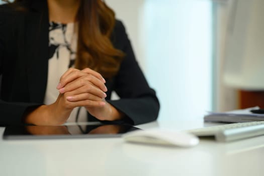 Businesswoman sitting at desk with hands clasped showing power and confidence during virtual remote online job interview.