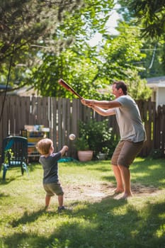 Father and son enjoying a game of baseball in their lush green backyard on a sunny day