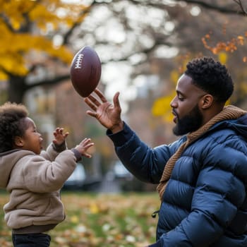 Father in a winter jacket handing a football to his excited young son in a leaf-strewn park