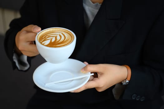 Close up shot of young woman holding a cup of coffee with latte art.