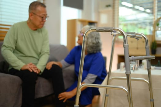 A metal walking frame against blurred doctor comforting upset senior patient during home visit.