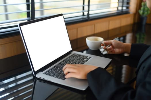 Female freelancer working and typing on laptop keyboard while sitting at modern coffee shop.