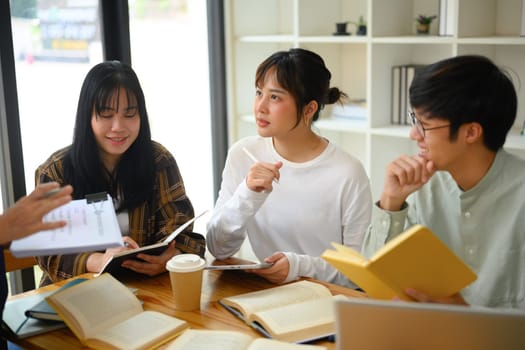 Group of college students sitting around a table in library and discussing research.