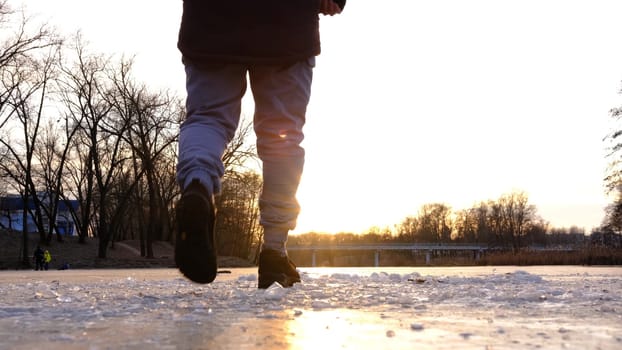 The lonely figure of a man walking on the frozen river at sunset, with peace of crystals ice in forward line , the reflection of the sun on the ice