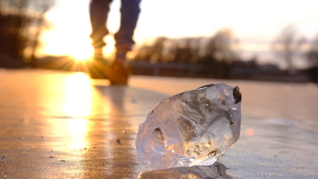 The lonely figure of a blured man walking on the frozen river at sunset, with peace of crystal ice in forward line, the reflection of the sun