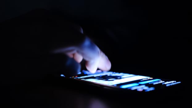 Close up of man finger using and touching on smartphone screen with reflection and black background in the darkness. Social network surfing, instagram or facebook or tiktok.