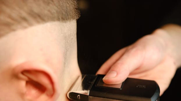 close up men's hairstyling and haircutting with barber shaving machine, hair cut for male. Hairdresser service with shaver in a modern barbershop in a dark key lightning with warm light side view.