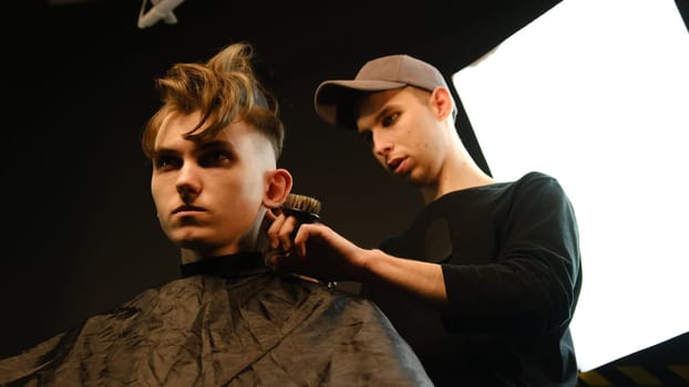 men's hairstyling and haircutting with hair clipper in a barber shop or hair salon. Hairdresser service in a modern barbershop in a dark key lightning with warm light low angle view.