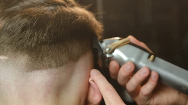 close up men's hairstyling and haircutting with hair clipper in a barber shop or hair salon. Hairdresser service in a modern barbershop in a dark key lightning with warm light and smoke back view.