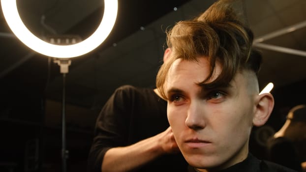 men's hairstyling and haircutting with hair clipper in a barber shop or hair salon. Hairdresser service in a modern barbershop in a dark key lightning with warm light front view.