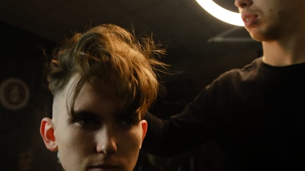 Barber shop. Man in barber's chair, hairdresser shaking hairs by the hand before cut and styling it. Concept Barbershop. front view in dark key lightning with warm light.