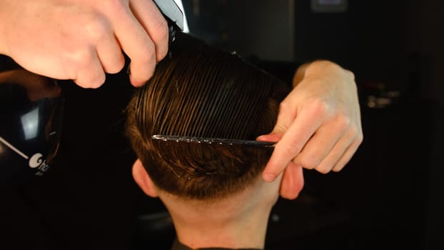 Spraying hair. barber spraying water on the hair of the client and comb it for cutting and styling. Concept Barbershop. back view in dark key lightning with warm light.