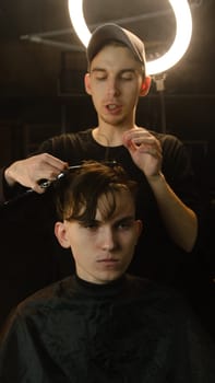 Barber master hairdresser does hairstyle and style with scissors and comb. Concept Barbershop. front view in dark key lightning with warm light.