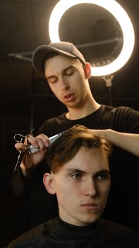 Barber master hairdresser does hairstyle and style with scissors and comb. Concept Barbershop. front view in dark key lightning with warm light.