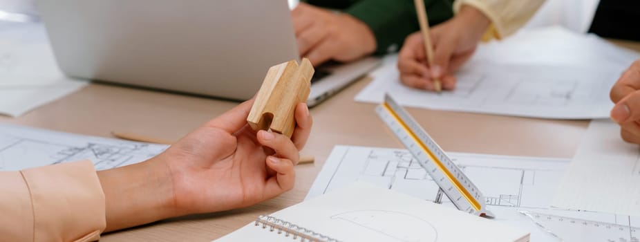 Professional architect team discussion about architectural project on meeting table with blueprint and wooden block scatter around at modern office. Closeup. Focus on hand. Delineation.