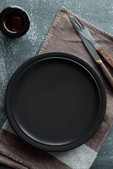 Black empty plate, cutlery and napkin on stone table top view. Table setting mock up. Vertical